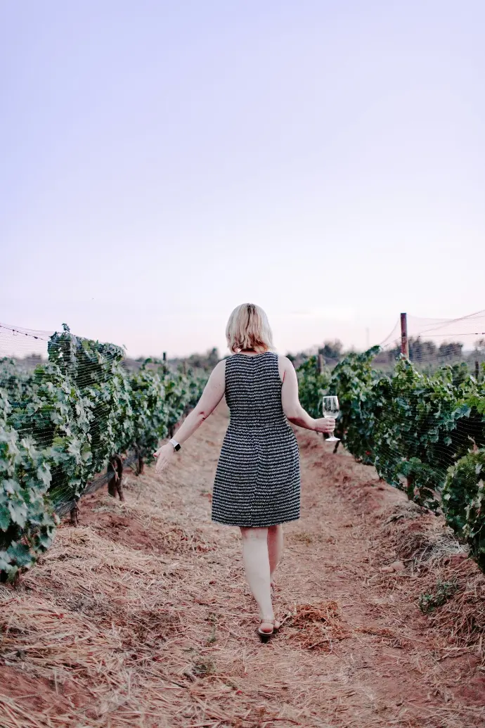 woman walking on vineyard holding wine glass